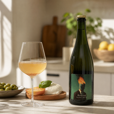 Botella de Anónimo Muscat Pet Nat junto a una copa ligeramente turbia