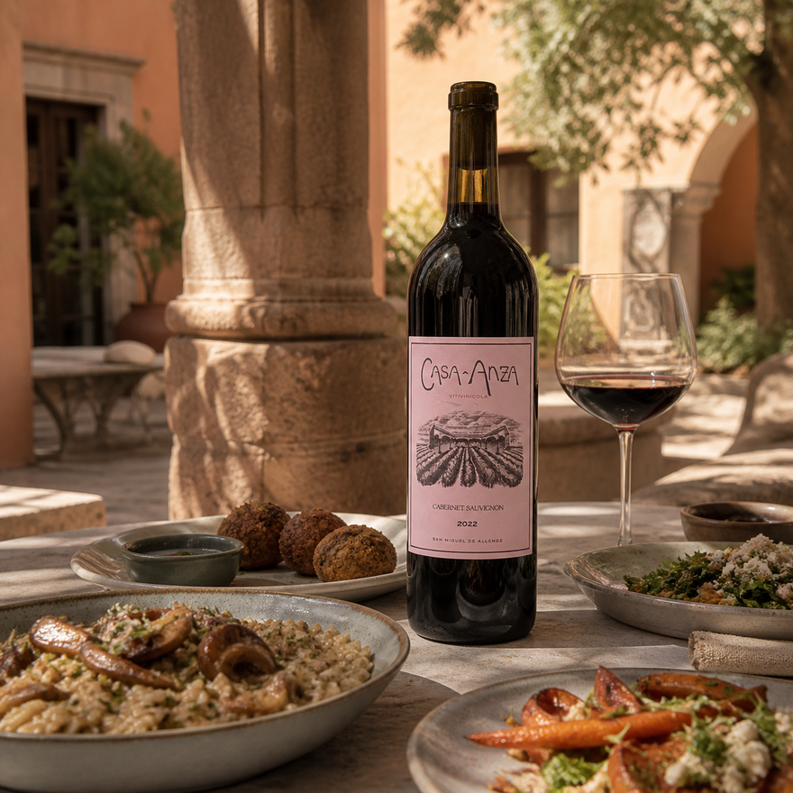 Botella de Casa Anza Cabernet Sauvignon sobre una mesa con risotto, falafel y vegetales en un patio de San Miguel de Allende